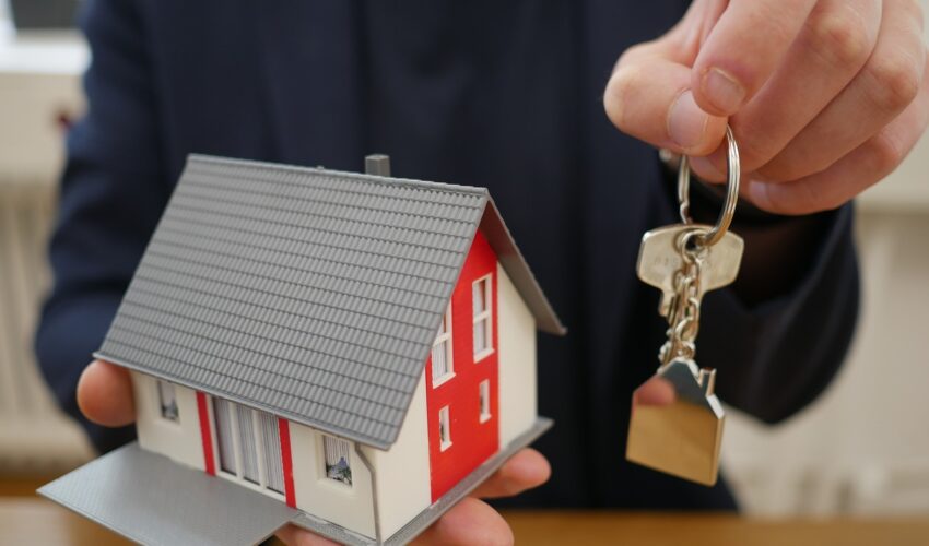 A person holding a model house and keys, representing real estate or home ownership.