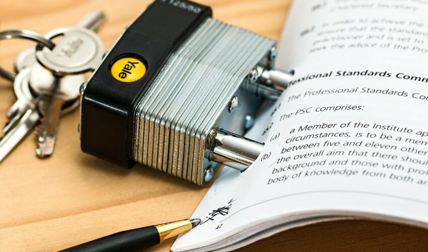 The image features a Yale Professional padlock with its keys placed on an open book that appears to be a legal document, with text visible about "Professional Standards Comm." A pen is positioned near the book.