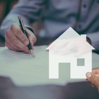 Two hands are shown, one holding a paper cutout of a house and the other holding a pen over a document, related to real estate or a mortgage.