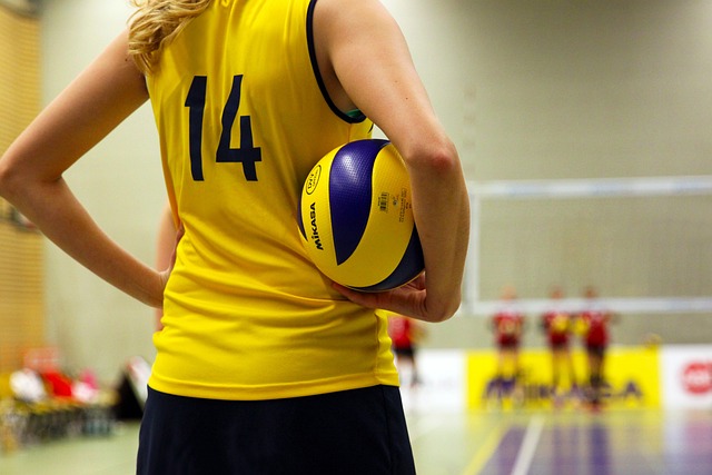A volleyball player in a yellow jersey with the number 14 holds a blue and yellow Mikasa volleyball.