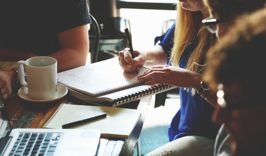 Three people collaborate with notebooks and a laptop at a table.