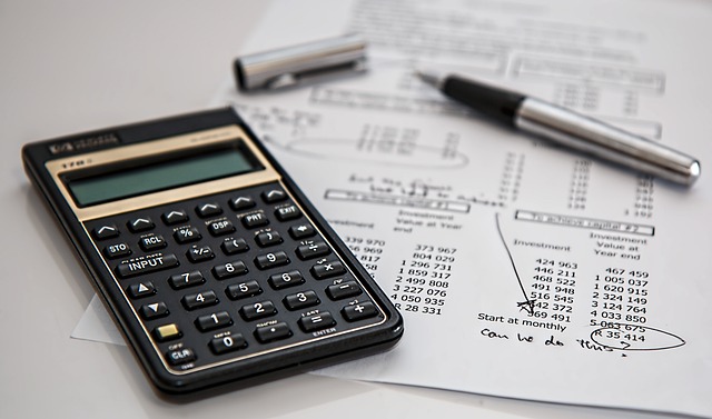 A calculator, pen, and financial documents are arranged on a desk, suggesting accounting or financial work.