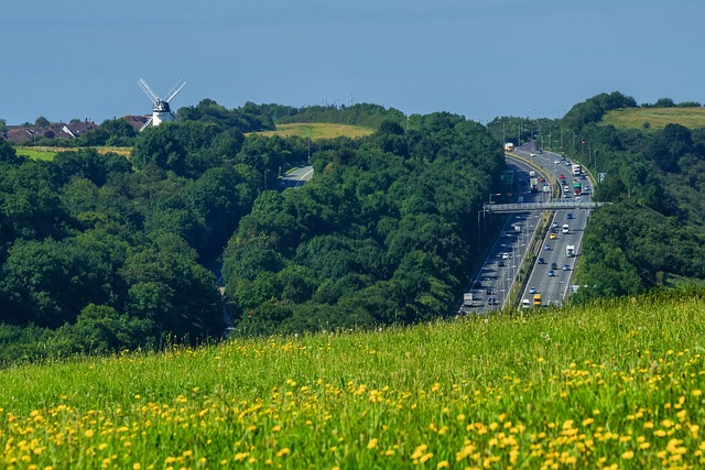 A highway winding through a green landscape with a windmill in the distance.