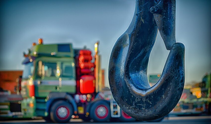 A large metal hook in the foreground with a blurry truck in the background.