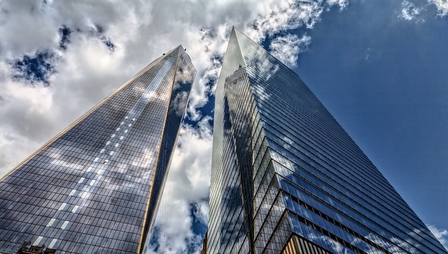 Two tall skyscrapers with reflective glass exteriors pointing towards a cloudy sky.