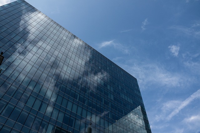 A low angle view of a glass-clad building reflecting a blue sky with wispy clouds.