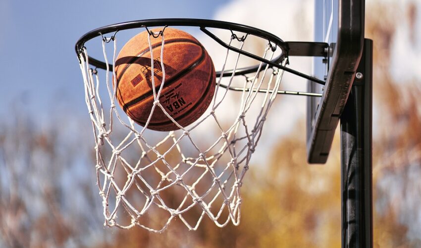 A basketball going through a net on an outdoor hoop.