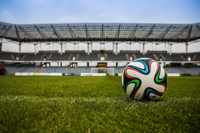 A soccer ball on a green field in front of an empty stadium.
